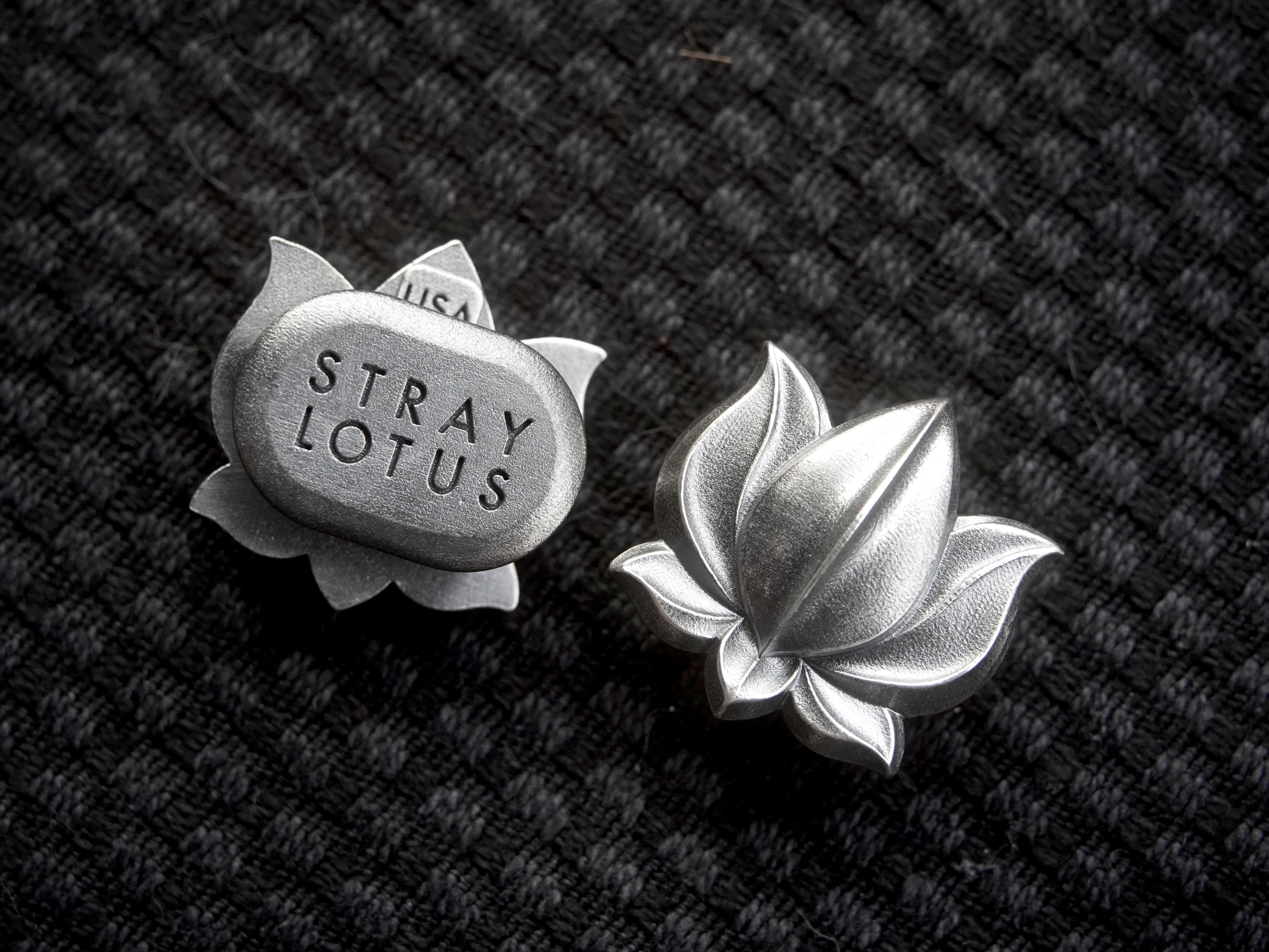 Two sterling silver Stray Lotus pins — the stamped reverse and the lotus face — on dark knit