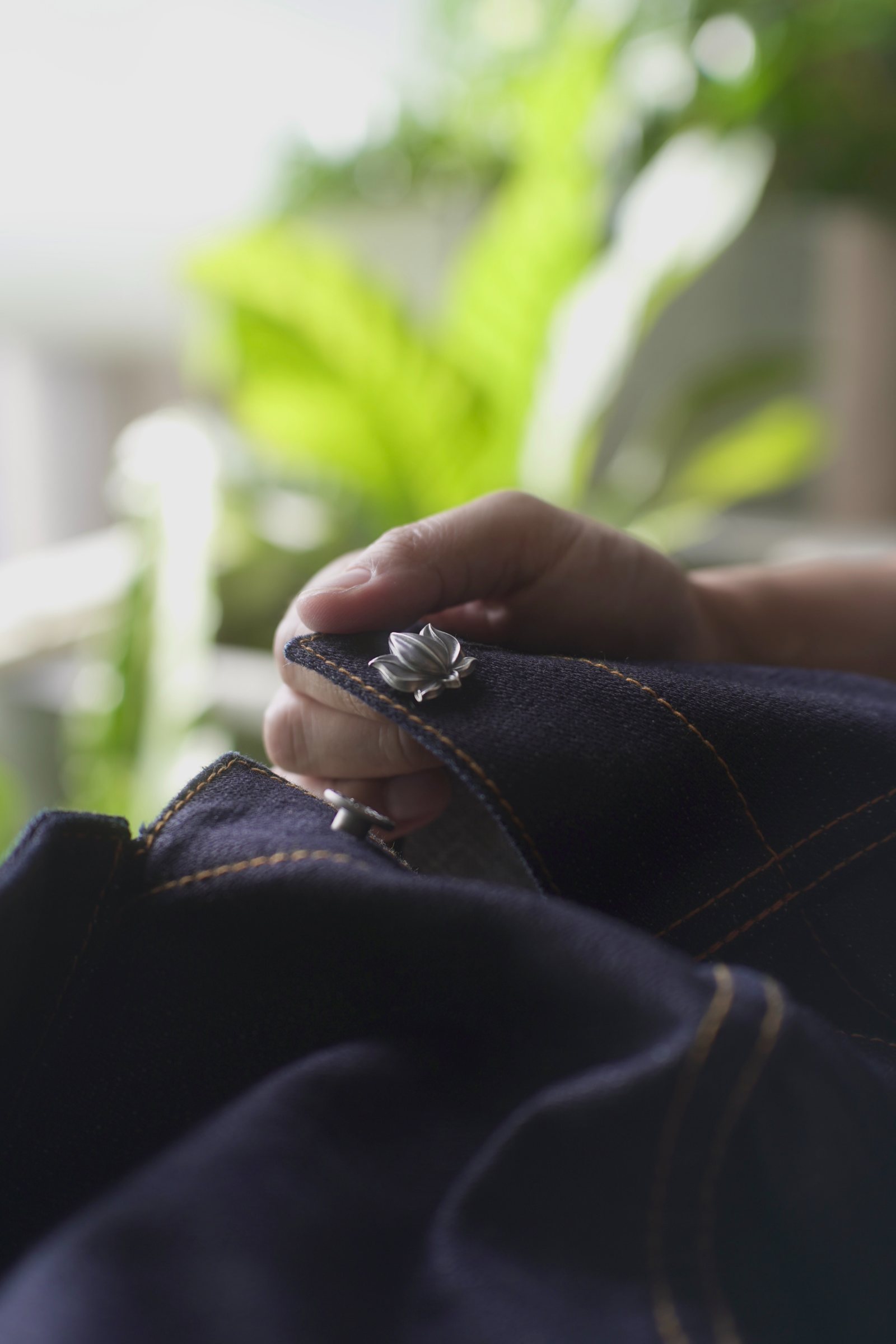 Lotus 001 in sterling silver held in the buttonhole of an indigo denim jacket