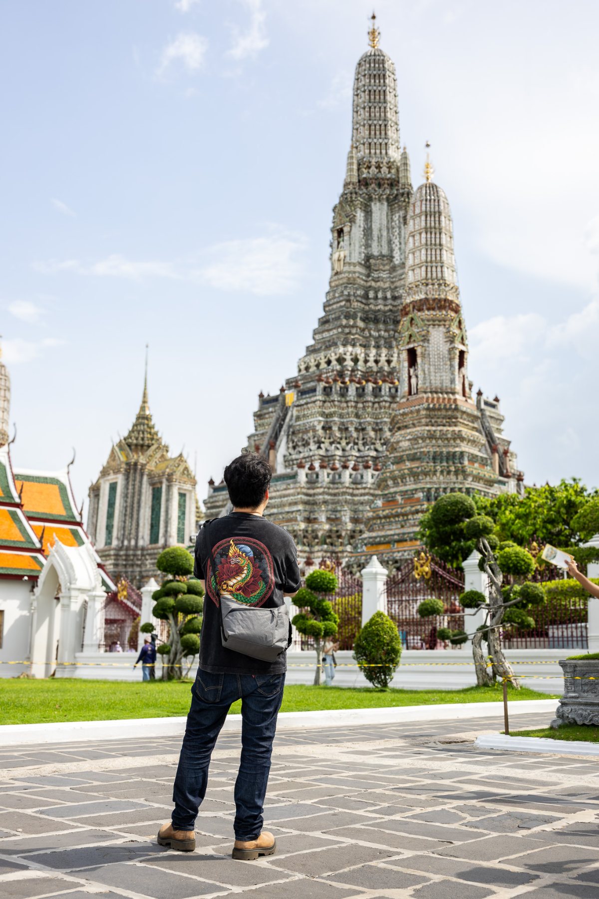 A man in denim standing before a tiled spire under a bright sky