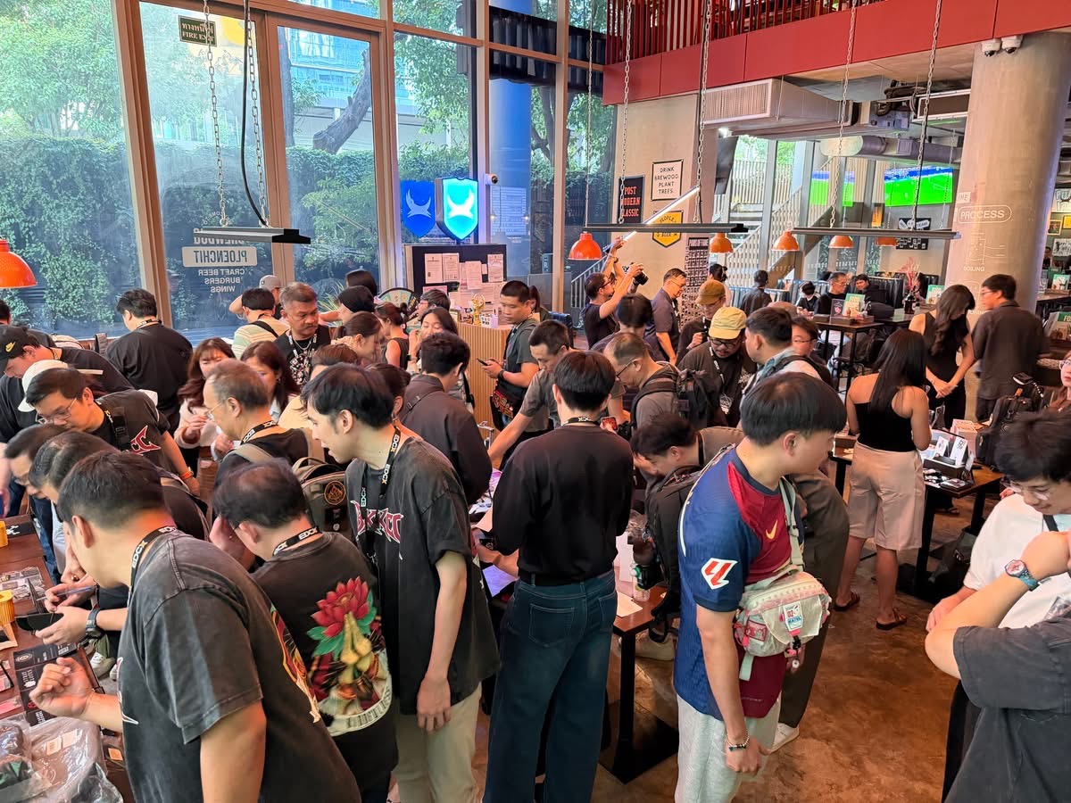 A dense crowd filling a glass-walled room around display tables