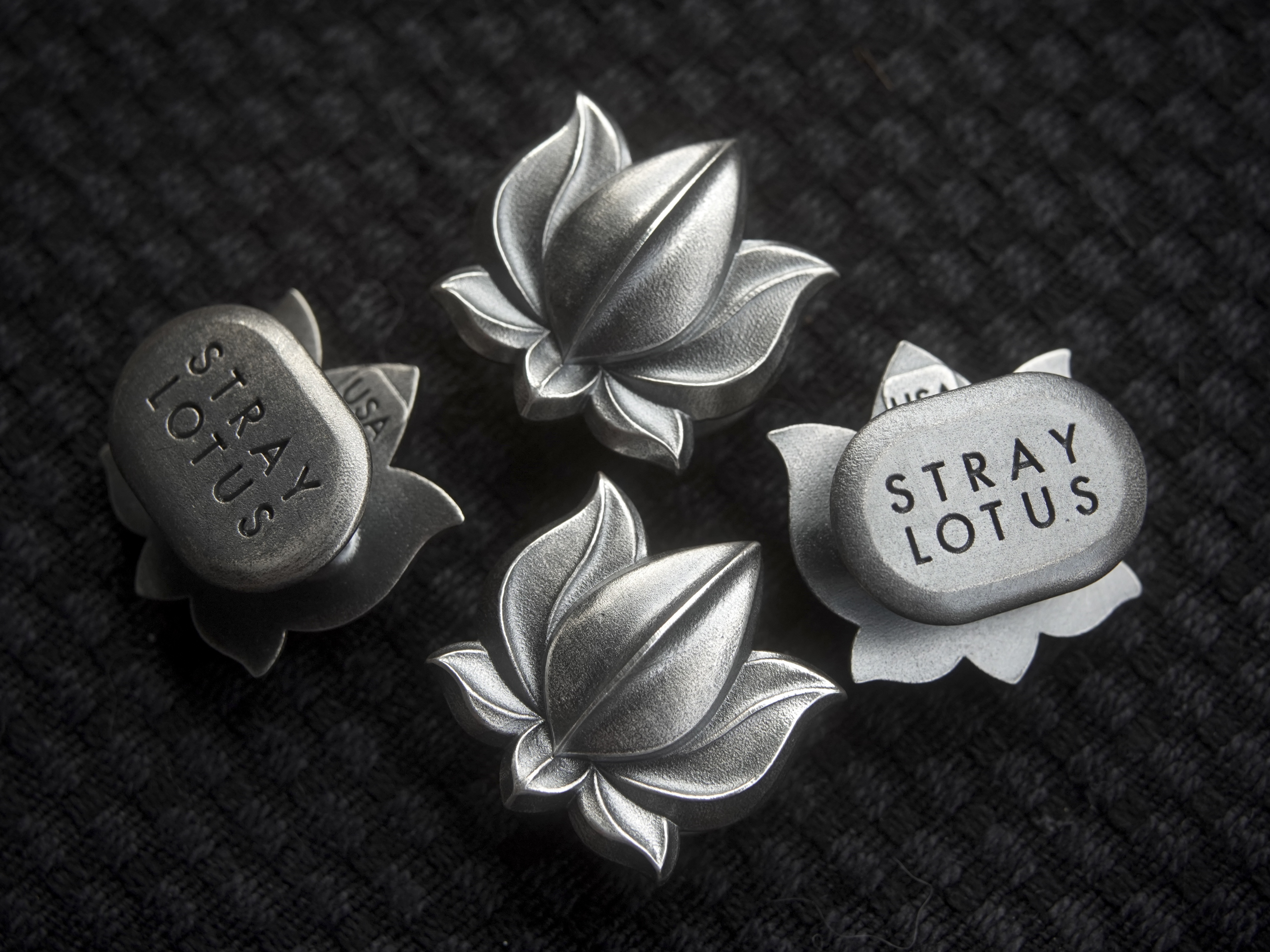 Four .925 sterling silver Stray Lotus pieces — lotus faces and STRAY LOTUS stamped reverses — on dark knit
