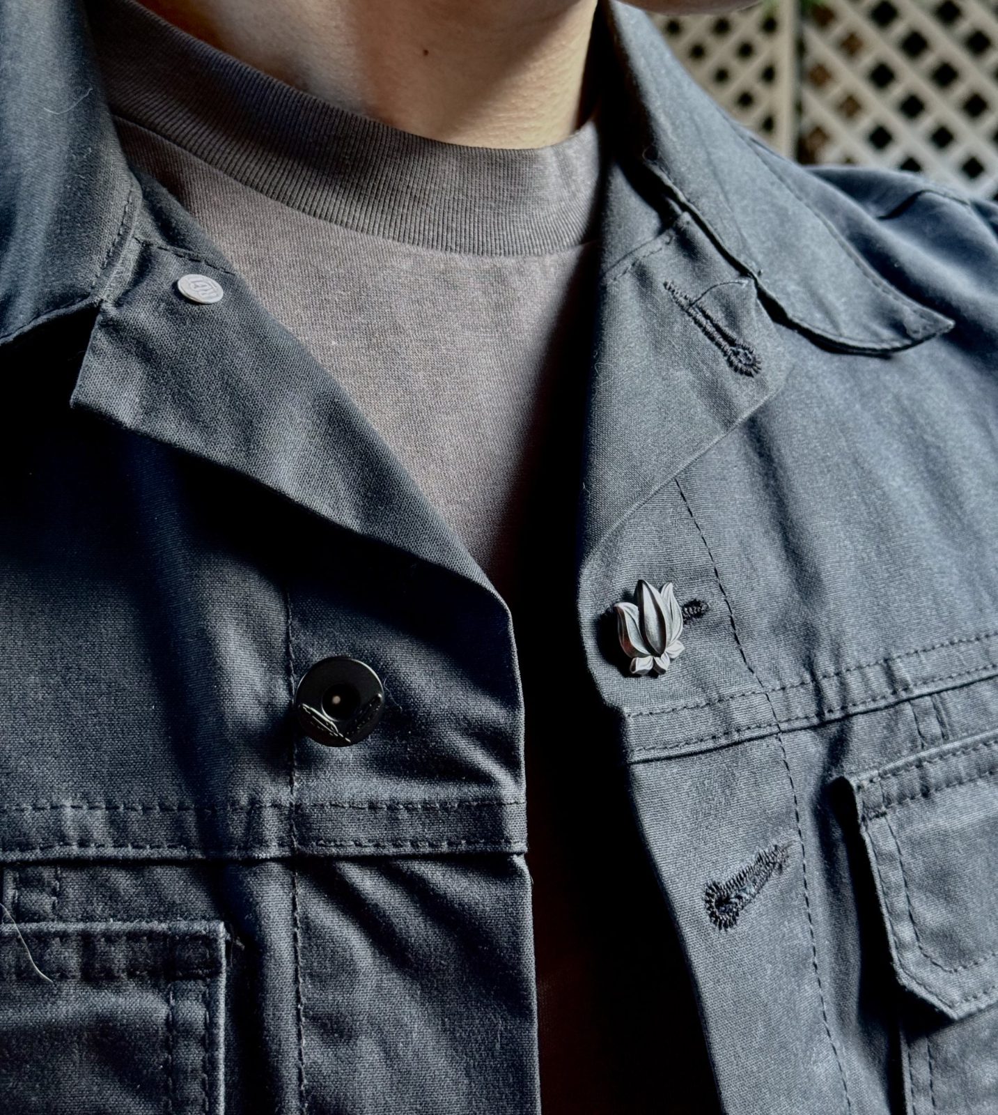 Lotus 001 in sterling silver worn in the buttonhole of a grey work jacket